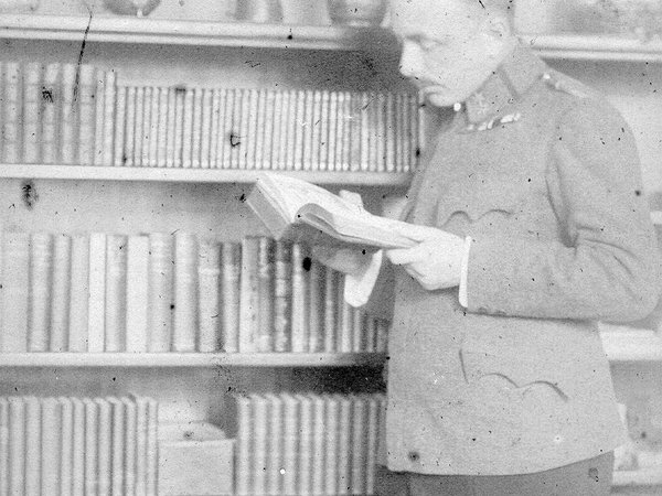 Fotografische Aufnahme in schwarz-weiß von Victor von Klemperer aus dem Jahr 1916. Er steht in Militäruniform vor einem gefüllten Bücherregal. In den Händen hält er ein geöffnetes Buch in dem er zu Lesen scheint.