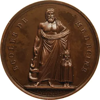 [Translate to English:] Bronze medal, the relief of which shows the holy Asclepius. On the right he holds a large, almost club-like staff towards the ground, with the snake coiling around it (Asclepius' or Asclepius' staff), in front of his left stands the small Telesphoros with hood and cape. The inscription reads: "ECOLES DE MEDECINE".