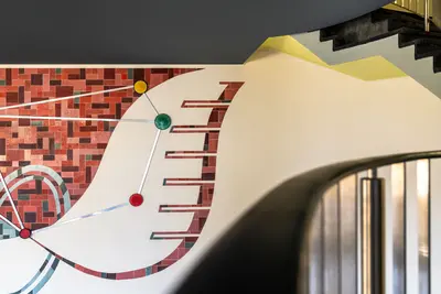 Wall decoration with red, brown and green tiles, metal lines and round elements in red, yellow and green.