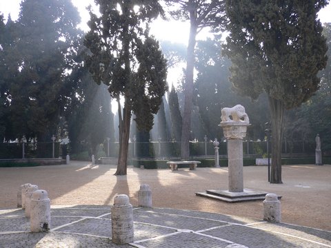 Der Hauptplatz der Villa Massimo mit Gartenanlage, kleinsteinigem Pflaster, steinernen Bänken und Säulen, auf denen Statuen von Tieren und Menschen tehen.
