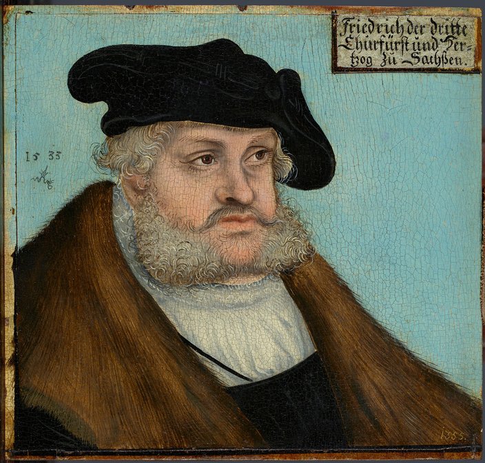 Portrait eines Mannes mit Mütze und Mantel vor hellblauem Hintergrund