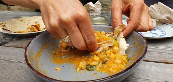 Zwei Hände schieben mit je einem Fetzen Brotfladen Curry auf einem Teller zusammen.