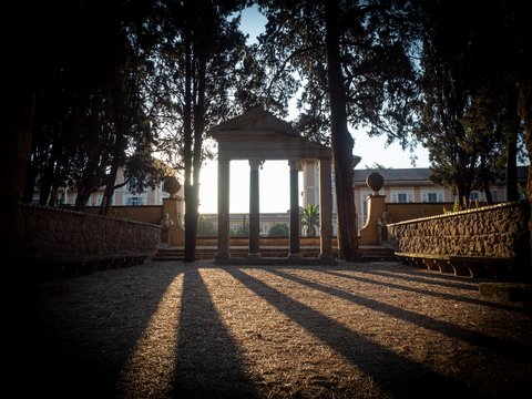 hohe Bäume und ein Säulenportal, das an eine antike Tempelanlage erinnert, werfen lange Schlagschatten in den Garten der Villa Massimo