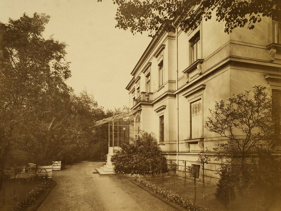 Historische Sepiafotografie der Villa von Klemperer in der Wiener Straße 25. Auf dem Foto ist der Eingang des Hauses zur Rechten neben einem Schotterweg und hohen Bäumen abgebildet.