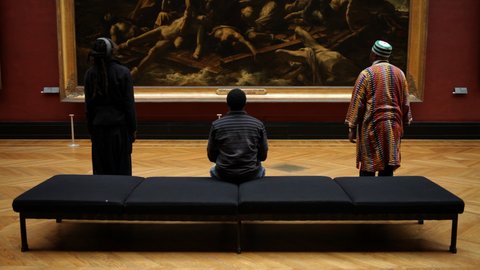 Rückansicht dreier Männer, die im Louvre Théodore Géricaults Gemälde &quot;Das Floß der Medusa&quot; besehen, dessen Unterkante mit einigen der Schiffbrüchigen im Hintergrund zu sehen ist.