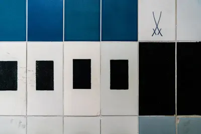 Gekreuzte Schwerter als Logo von Meißner Porzellan auf blauen, weißen und schwarzen rechteckigen Fliesen.