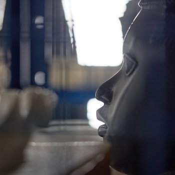 Eine Benin-Maske ist im Profil zu sehen, das Depot in dem sie gelagert ist, liegt in der Unschärfe