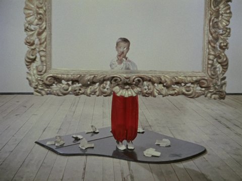 Ein Junge wirft Papierflieger durch einen riesigen barocken Bilderrahmen hindurch auf den Zuschauer zu.