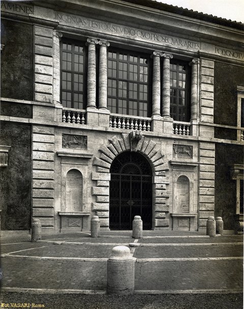 Eine Fotographie der Villa Massimo von 1914: Die steinerne unverputzte Front des Mittelteils der Villa, mit großem Eingangstor, das nach oben hin mit einem Rundbogen abschließt und der oberen Etage, die mit einer großen, fein gegliederten Fensterfront versehen ist, die von je zwei Säulenpaaren gesäumt ist.