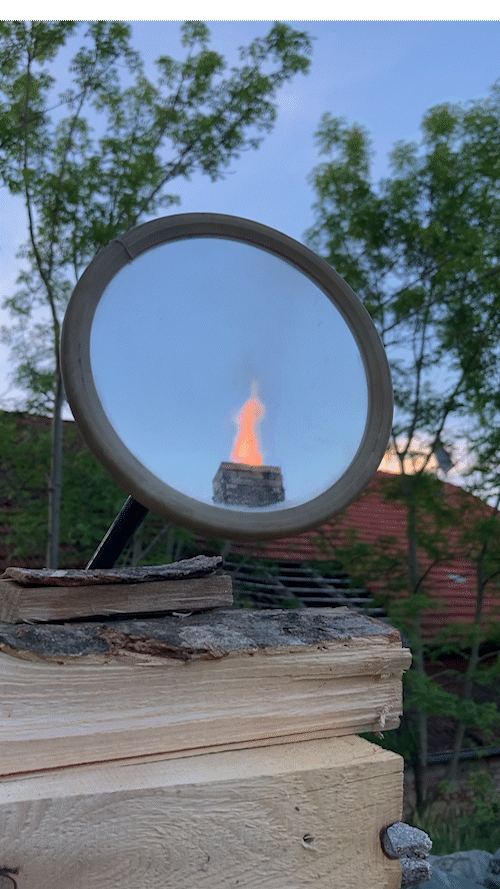 In einem runden Spiegel ist die lodernde Flamme vom Schornstein des Brennofens zu sehen.